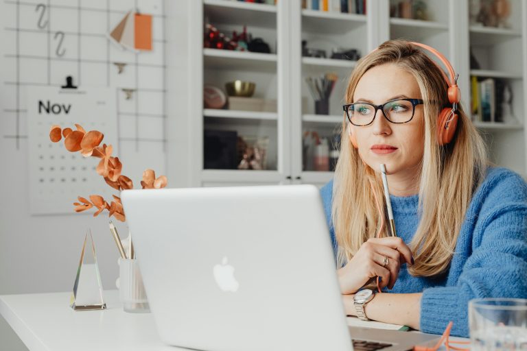 Thoughtful girl in front of a laptop holding a pen and using headphones